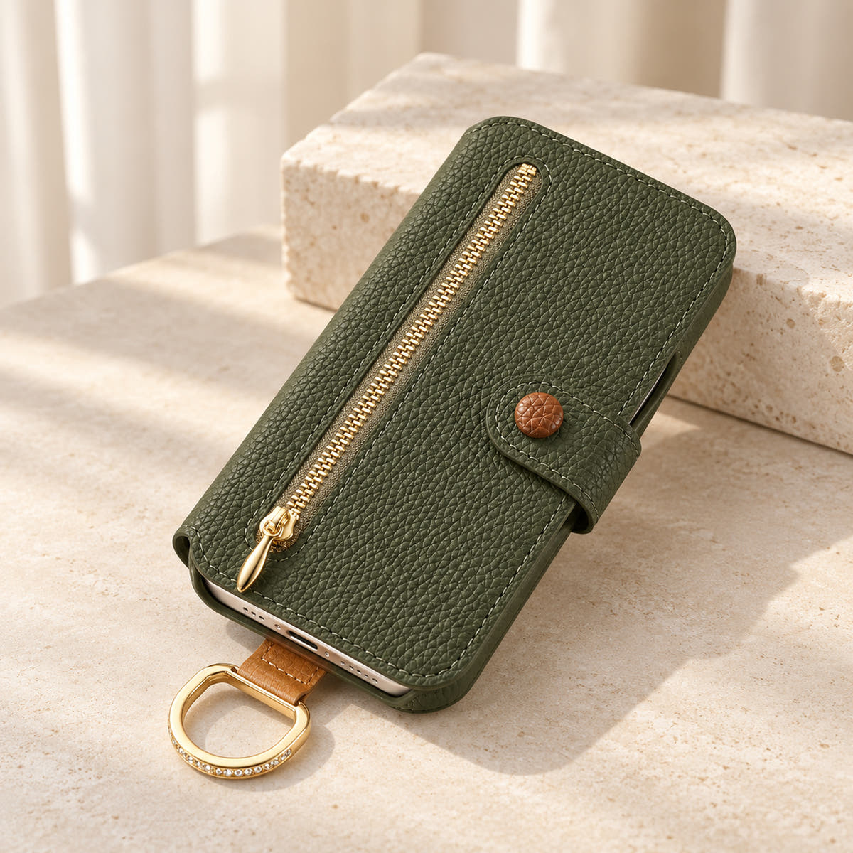 Forest Green textured iPhone wallet case closed on a cream surface, showing the front zip pocket, buttoned tab and attached gold-tone D-ring