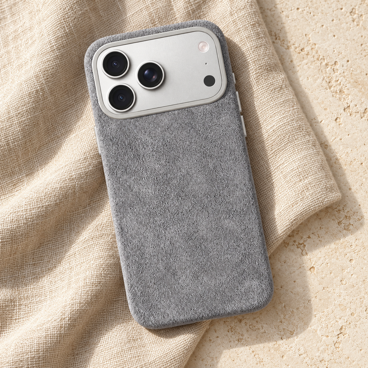 Light Grey suede-look textured iPhone case in a diagonal flatlay on oatmeal linen and cream stone.