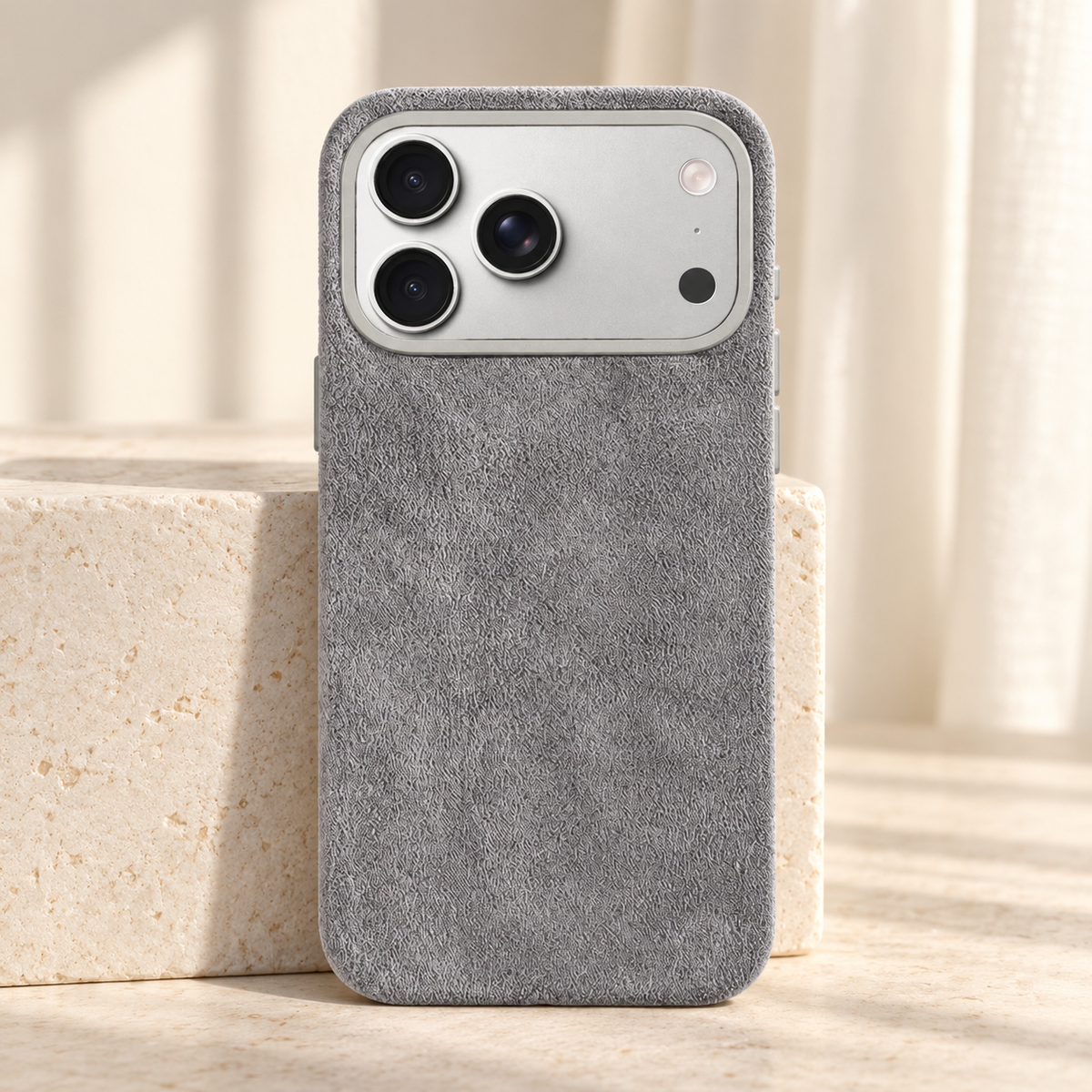 Light Grey suede-look textured iPhone case shown upright beside a pale stone block.