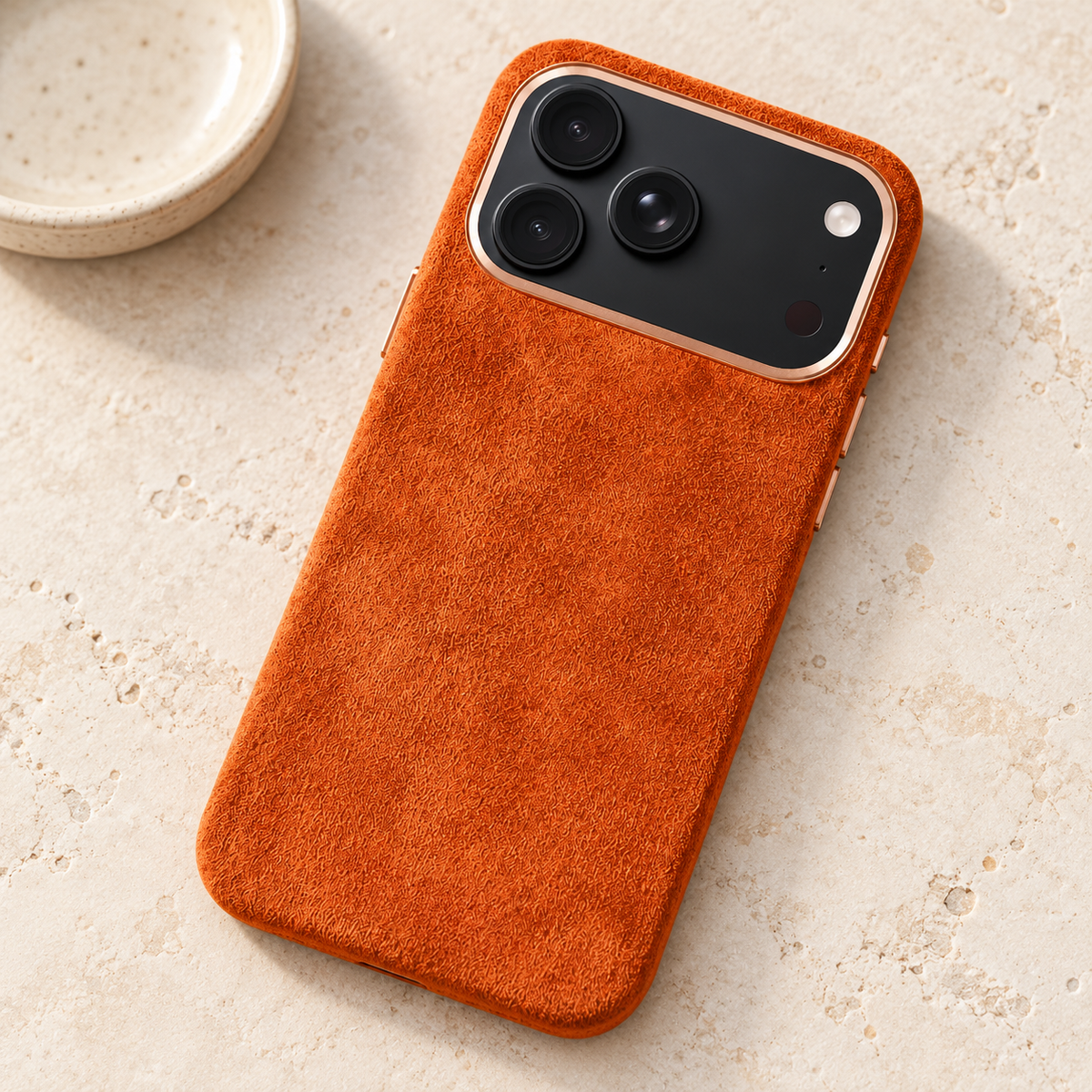 Burnt Orange suede-look textured iPhone case resting on a warm cream stone tabletop.
