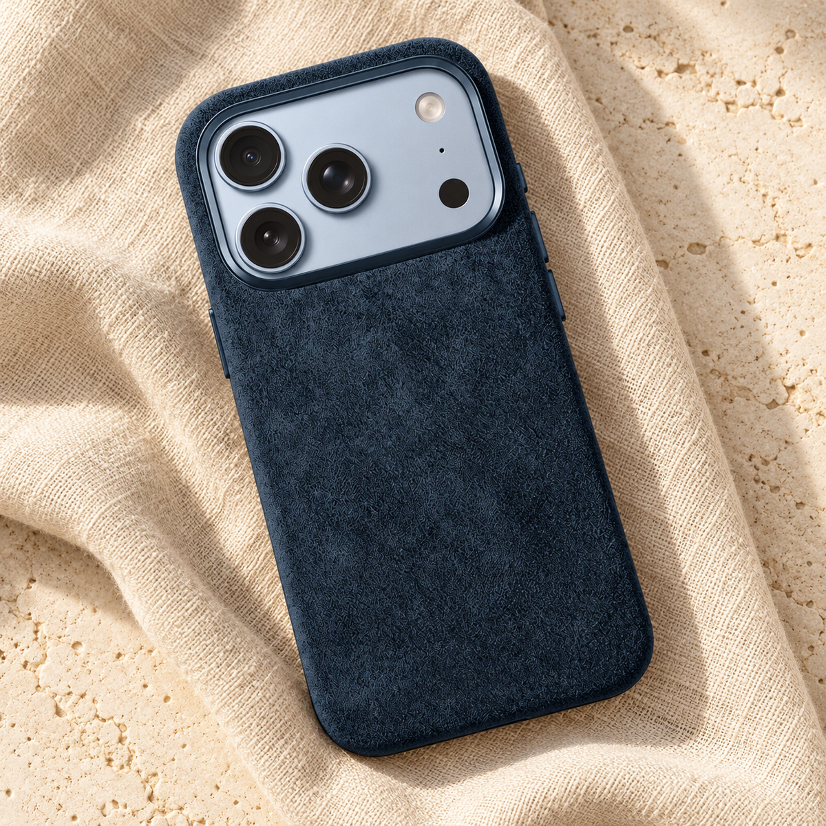Deep Navy suede-look textured iPhone case in a diagonal flatlay on oatmeal linen and cream stone.