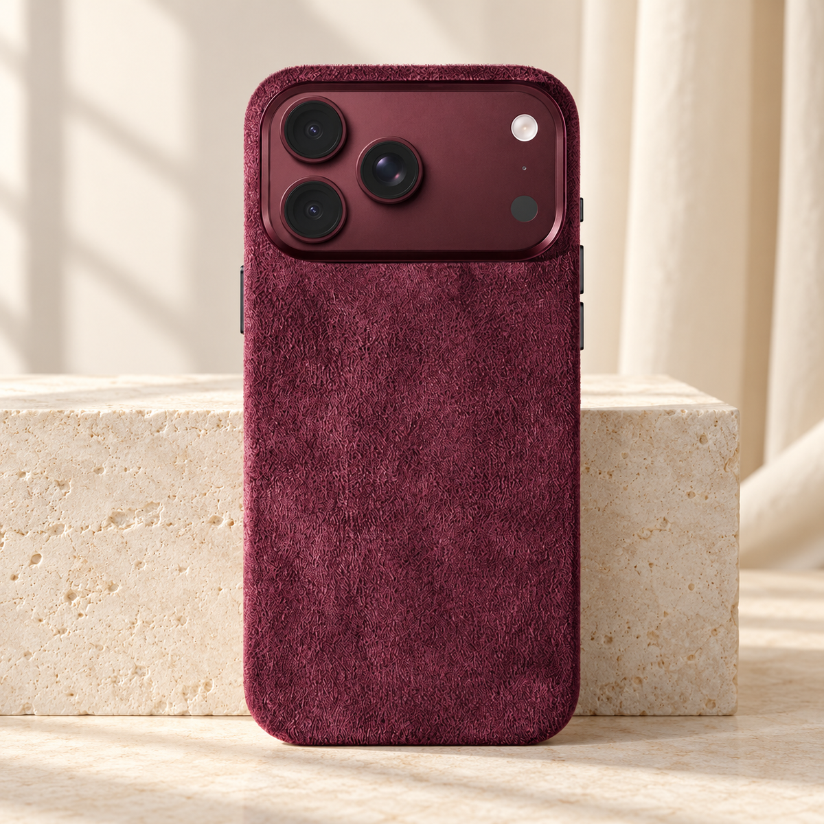 Burgundy suede-look textured iPhone case shown upright beside a pale stone block.