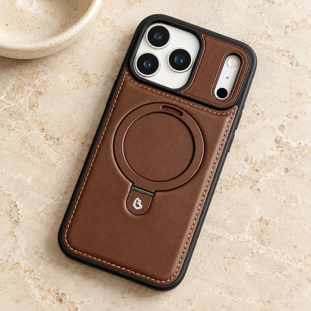 Brown stitched ring-stand iPhone case resting on a warm cream stone tabletop.