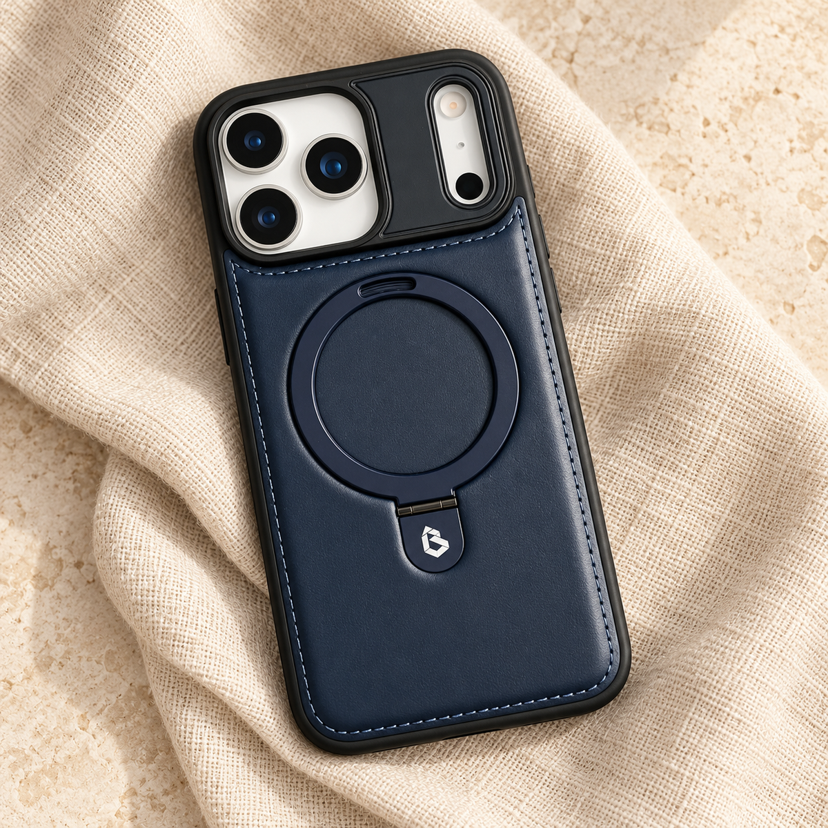 Navy stitched ring-stand iPhone case in a diagonal flatlay on oatmeal linen and cream stone.