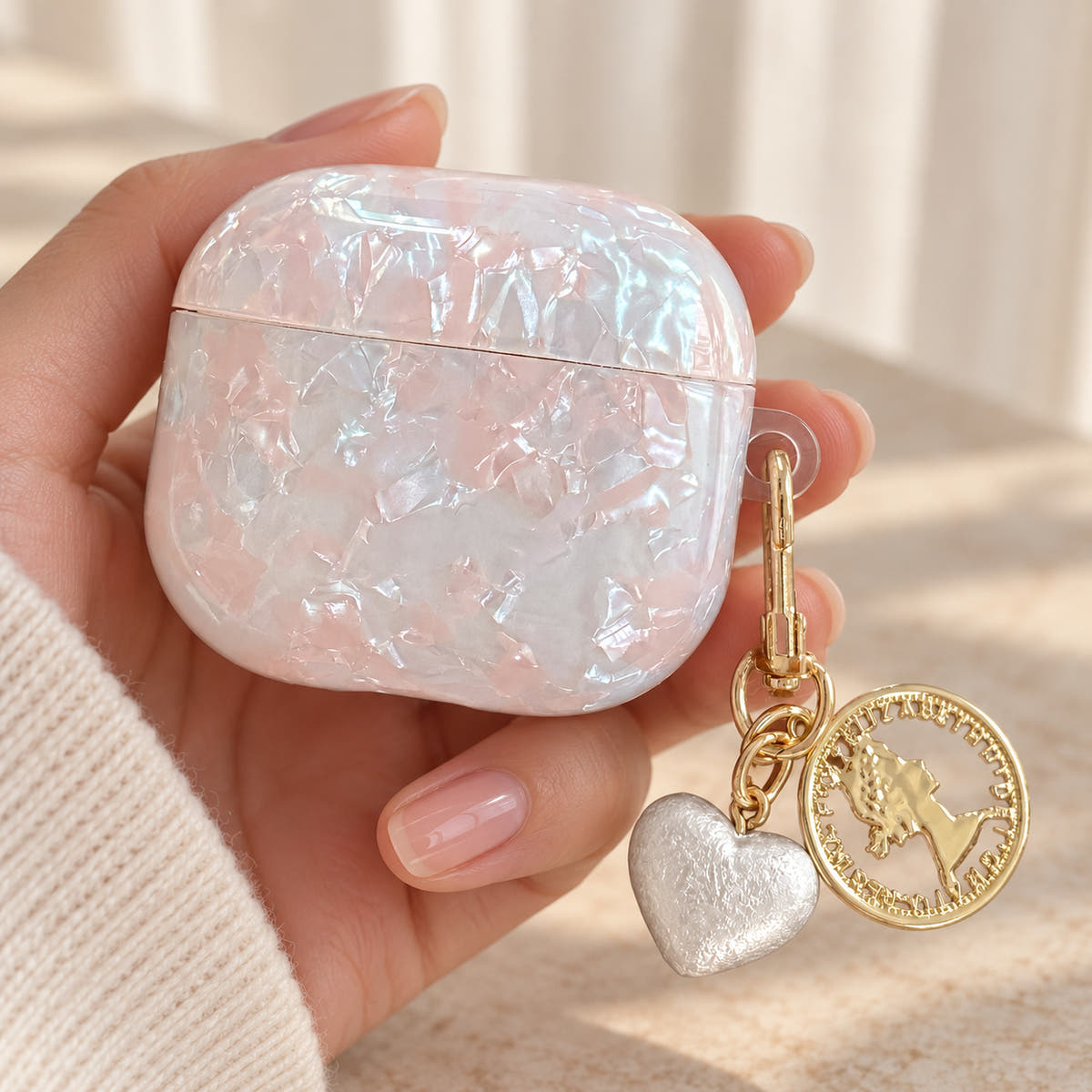 Opal Marble AirPods Case in Opal, hand detail with original attached charms on a warm cream background