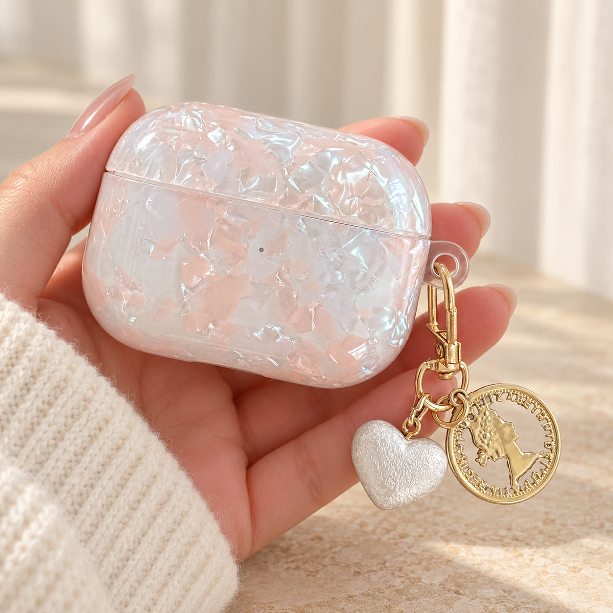 Opal Marble AirPods Case in Opal, in hand with original attached charms on a warm cream background