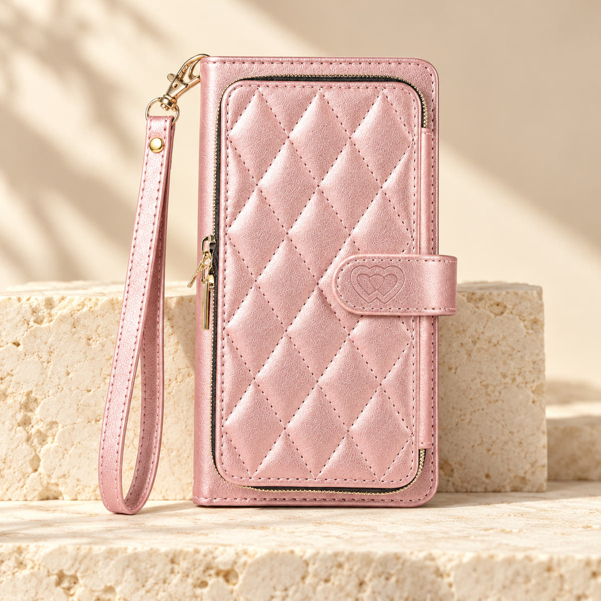 Pink padded zip iPhone wallet case with matching wrist strap on limestone