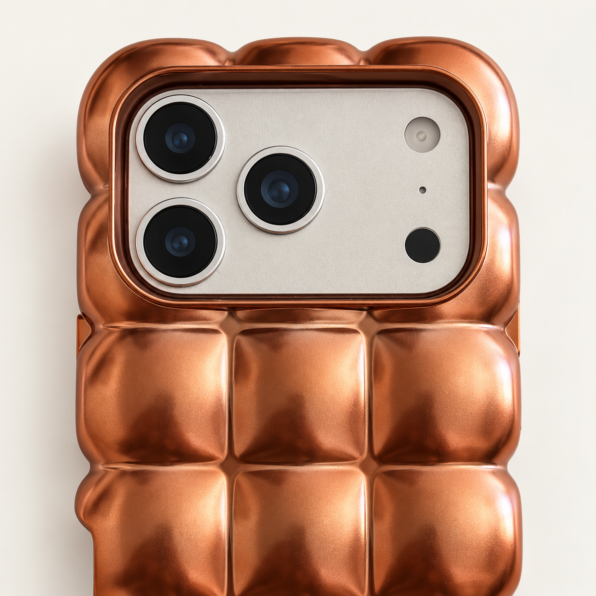 Copper puffy grid iPhone case with rounded-square back and scalloped edges — close-up of camera surround and sculpted grid.