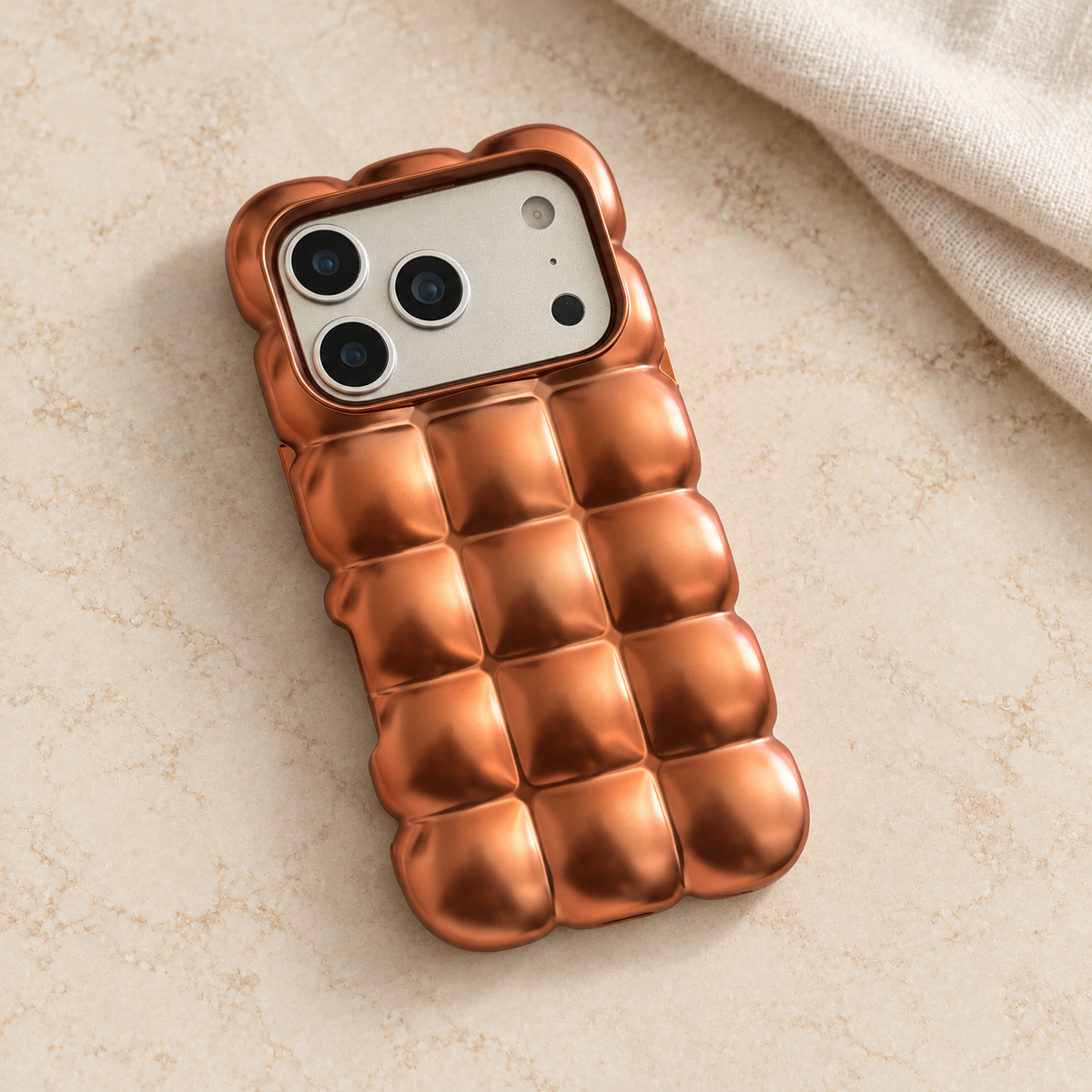 Copper puffy grid iPhone case with rounded-square back and scalloped edges — diagonal tabletop view.