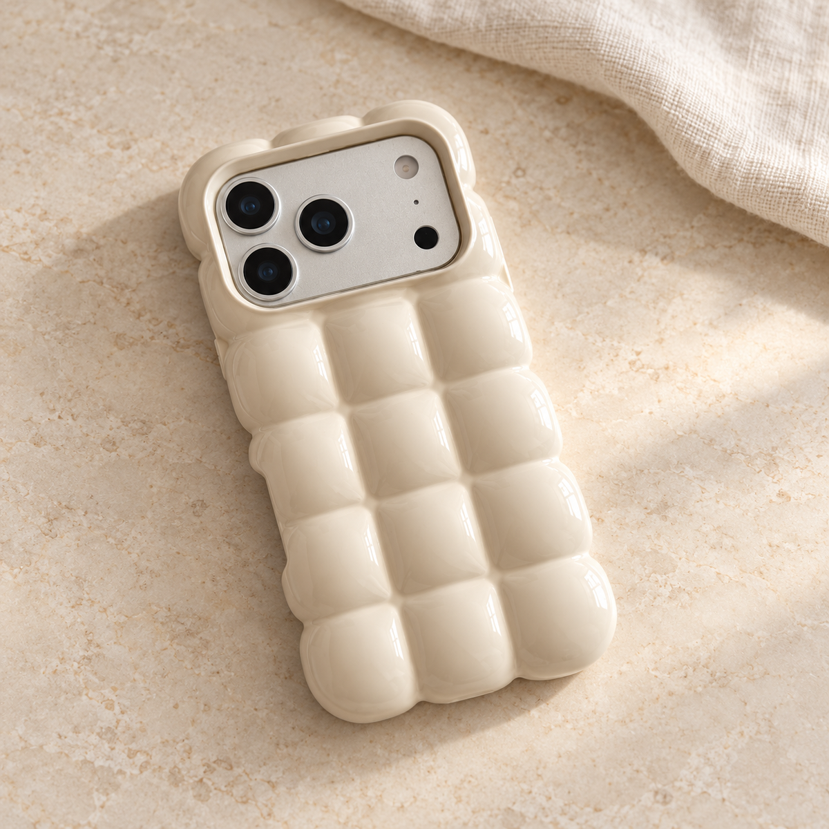 Cream puffy grid iPhone case with rounded-square back and scalloped edges — diagonal tabletop view.