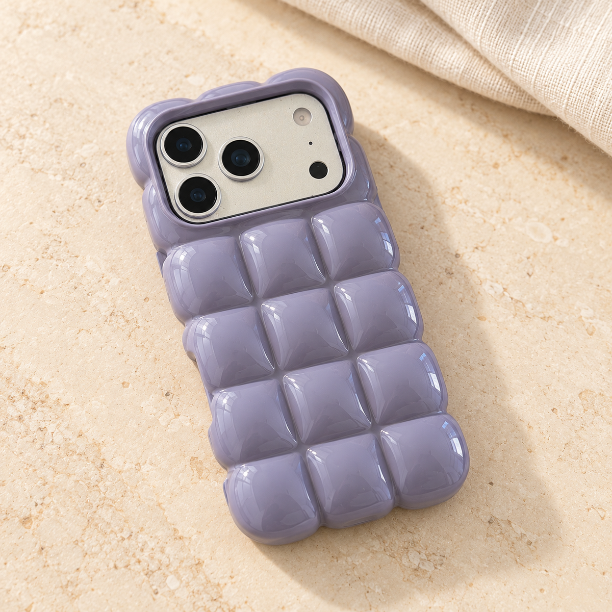 Lavender puffy grid iPhone case with rounded-square back and scalloped edges — diagonal tabletop view.