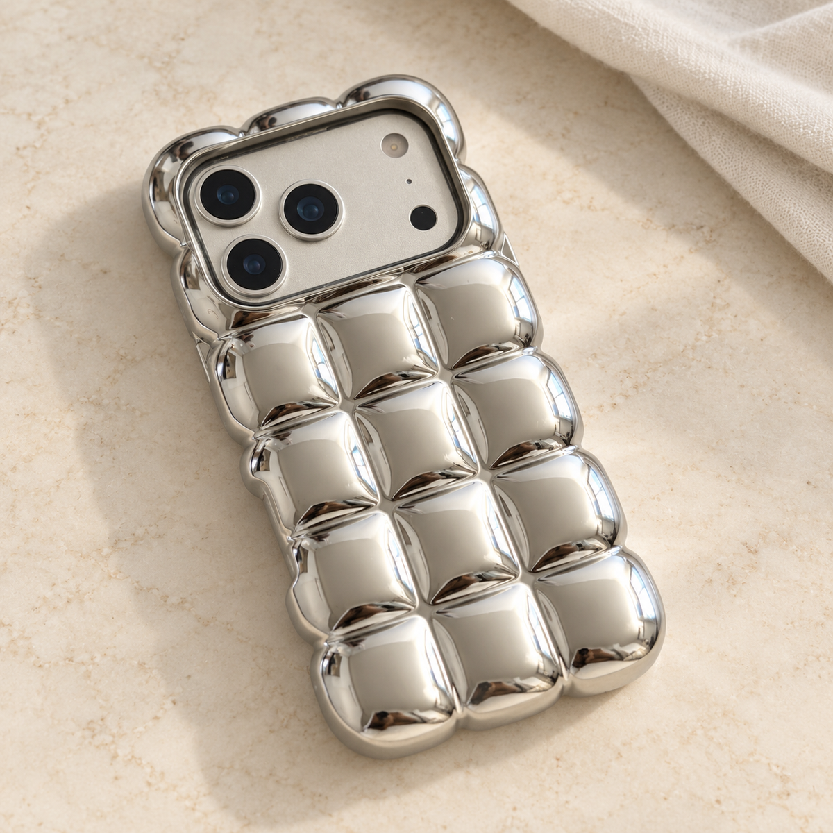 Mirror Silver puffy grid iPhone case with rounded-square back and scalloped edges — diagonal tabletop view.