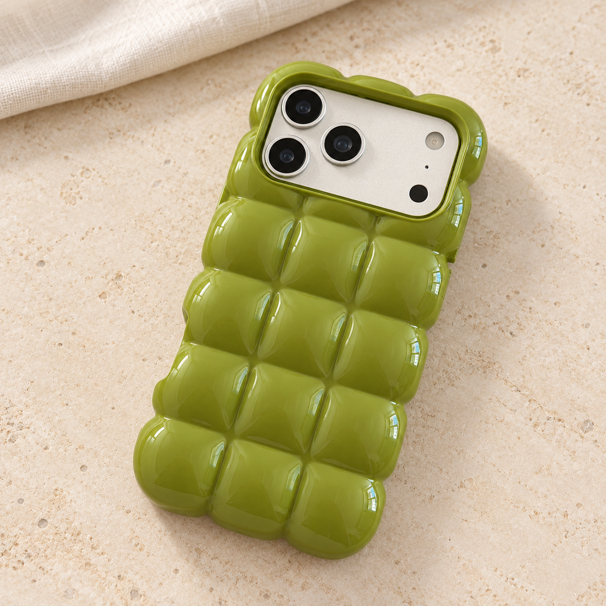 Olive Green puffy grid iPhone case with rounded-square back and scalloped edges — diagonal tabletop view.