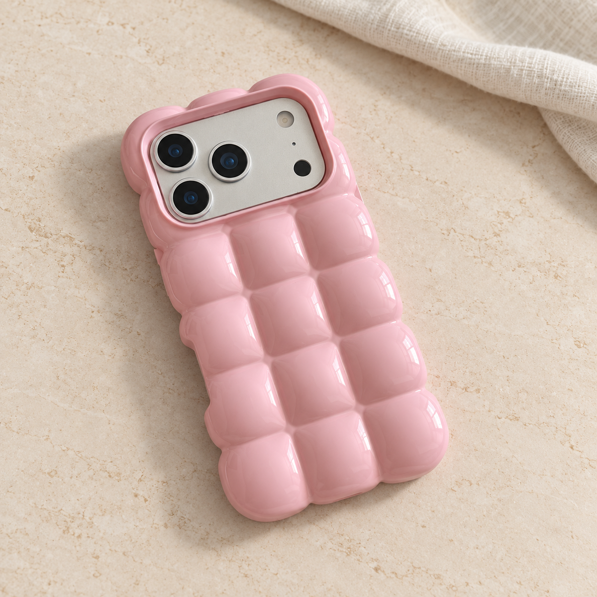 Pink puffy grid iPhone case with rounded-square back and scalloped edges — diagonal tabletop view.