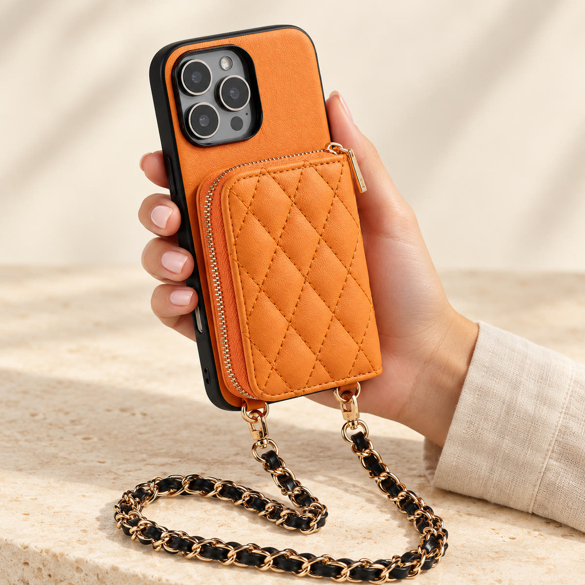 Orange quilted iPhone wallet case — handheld view with zip wallet and chain