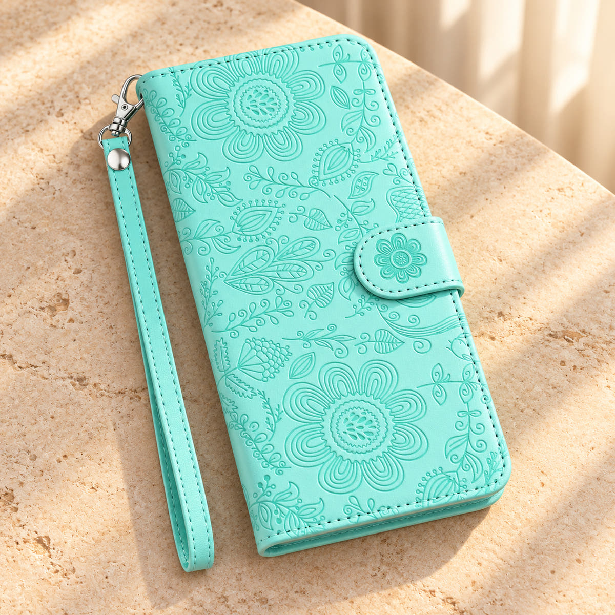 ScarletBloom Ice Blue floral wallet phone case on a cream tabletop, showing the full embossed front, flower closure and single-rivet wrist loop.