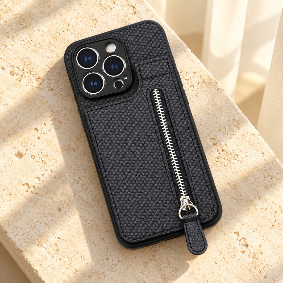 Signature Black iPhone wallet case resting on cream limestone with its complete textured back and silver-tone zipper visible.