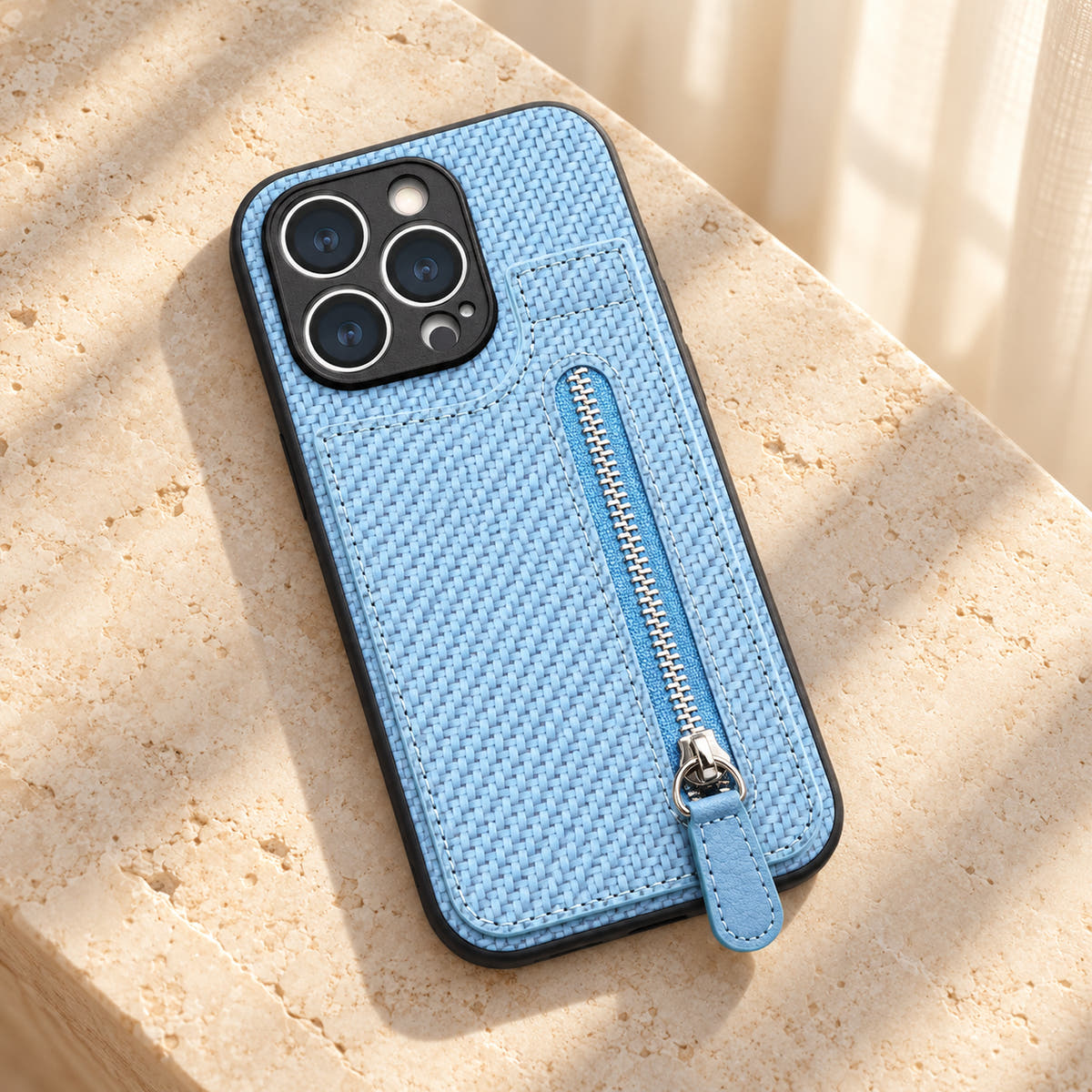 Signature Blue iPhone wallet case resting on cream limestone with its complete textured back and silver-tone zipper visible.