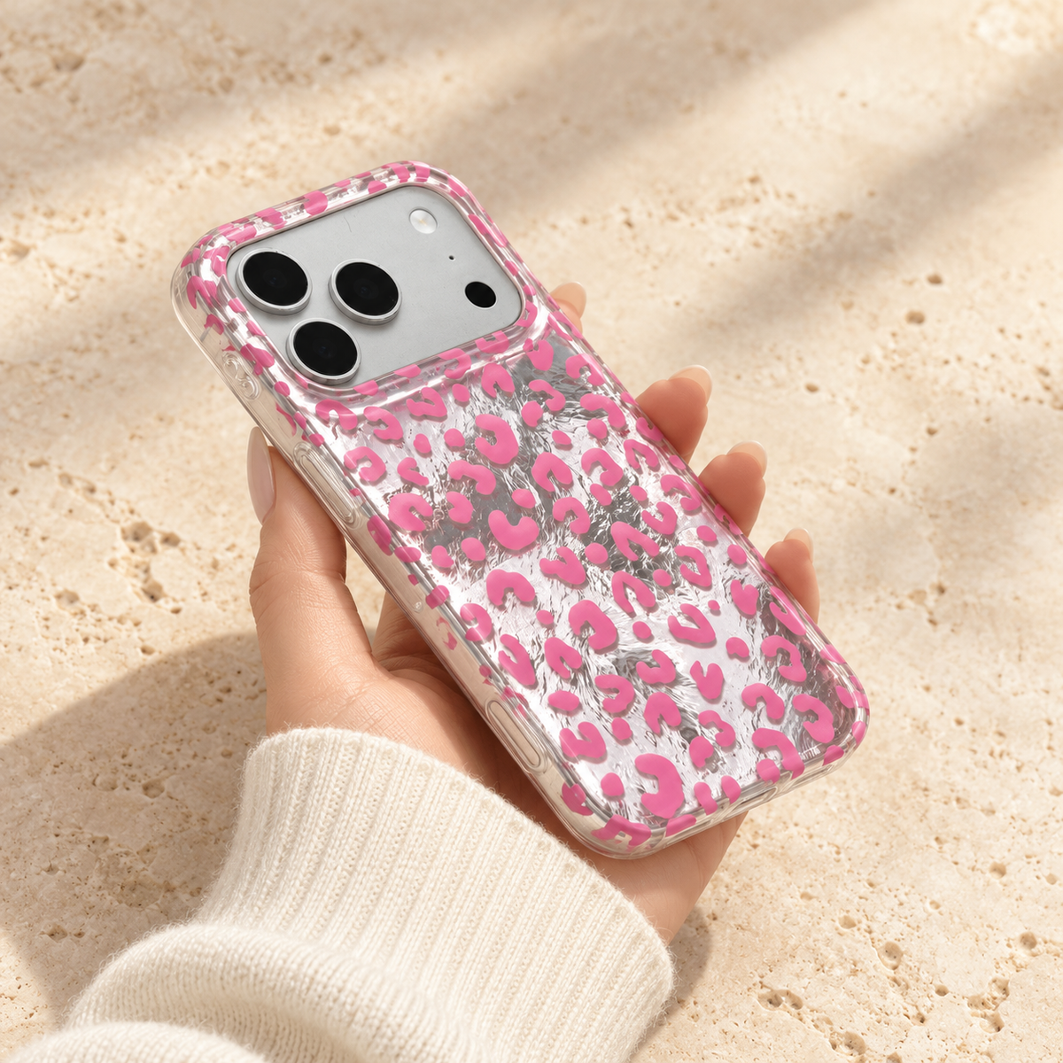 Pink leopard iPhone case held at a shallow angle to show its clear side edge and reflective back.