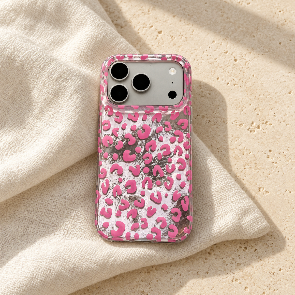 Pink leopard iPhone case styled on ivory linen with soft natural light across its silver-effect back.