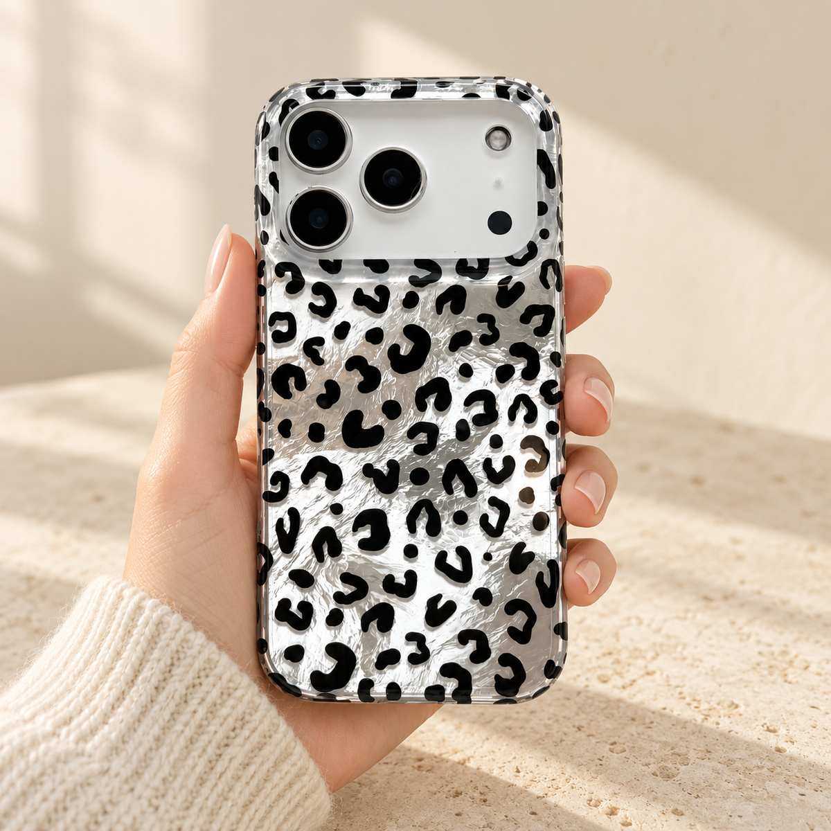 Black leopard iPhone case held upright in one hand, showing the crinkled silver finish and patterned clear rim.