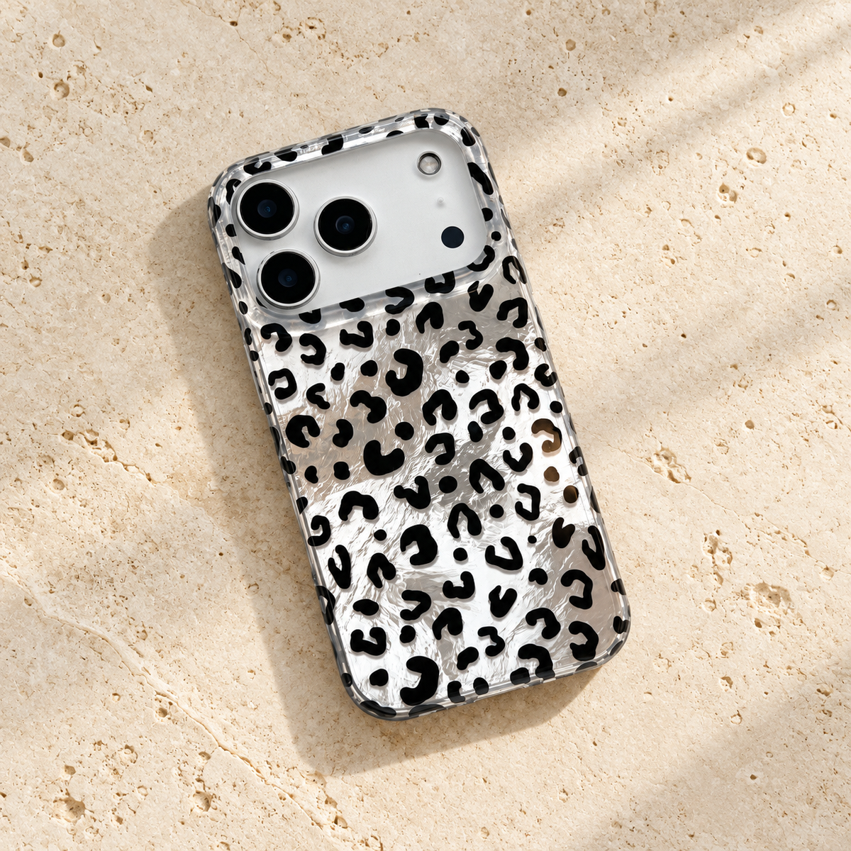 Black leopard iPhone case lying diagonally on a cream stone tabletop with its silver-effect back visible.