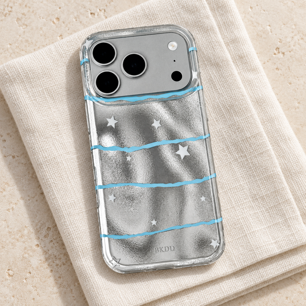 Silver Star Wave iPhone case resting on ivory linen with its reflective back and clear rim visible.