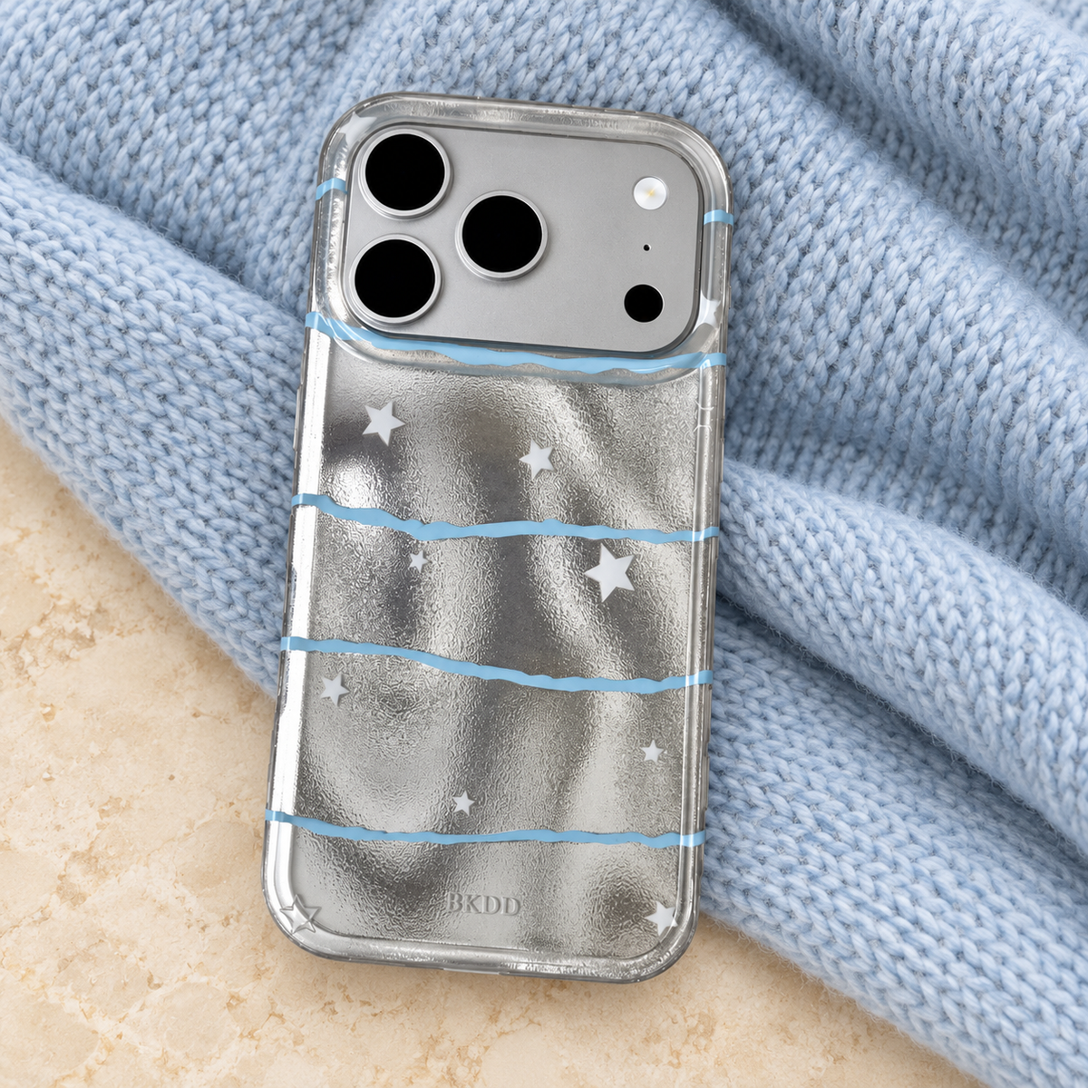 Silver Star Wave case resting on pale-blue knit fabric, showing its silver back and matching blue-wave print.