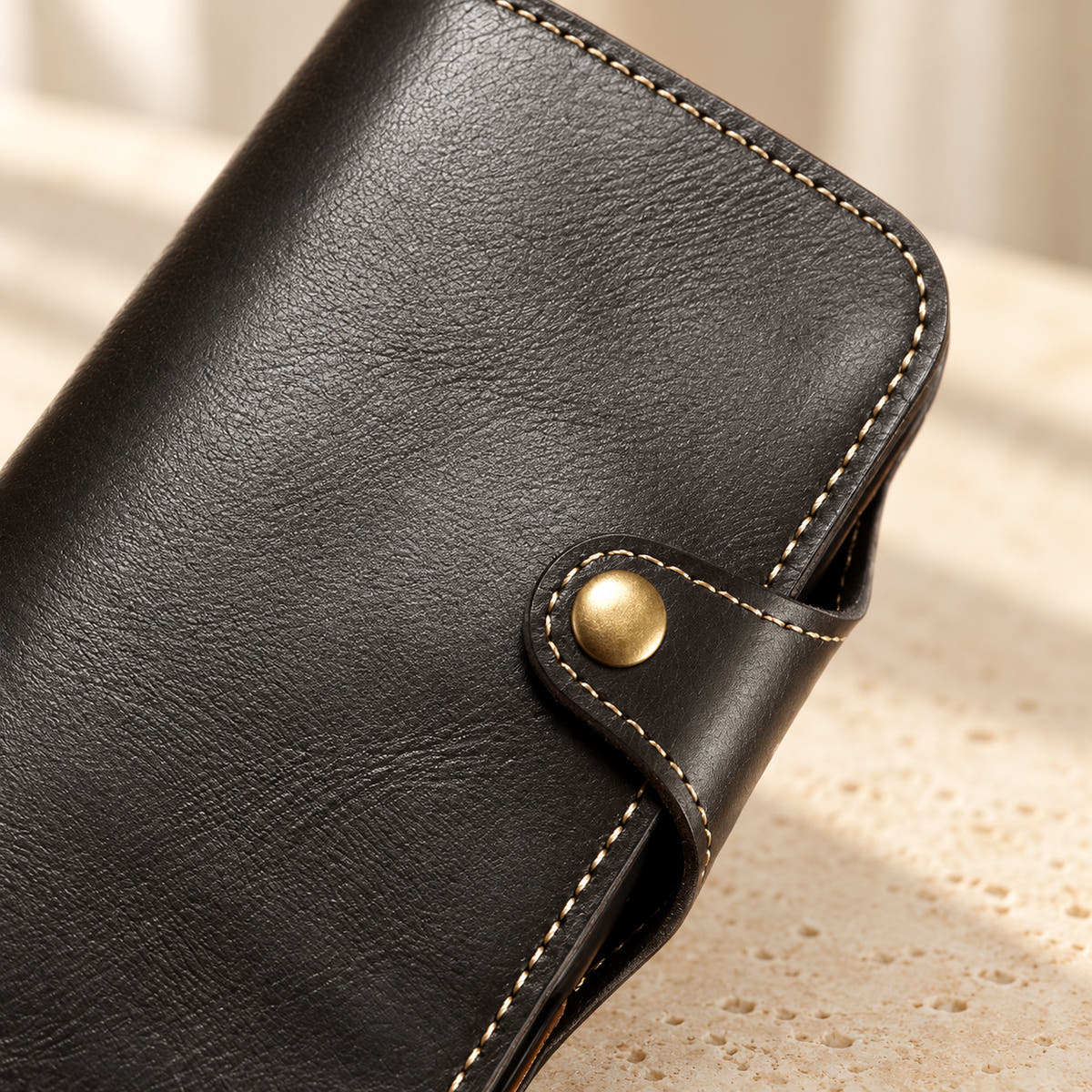 Close-up of the black wallet case button tab, contrast stitching and textured front