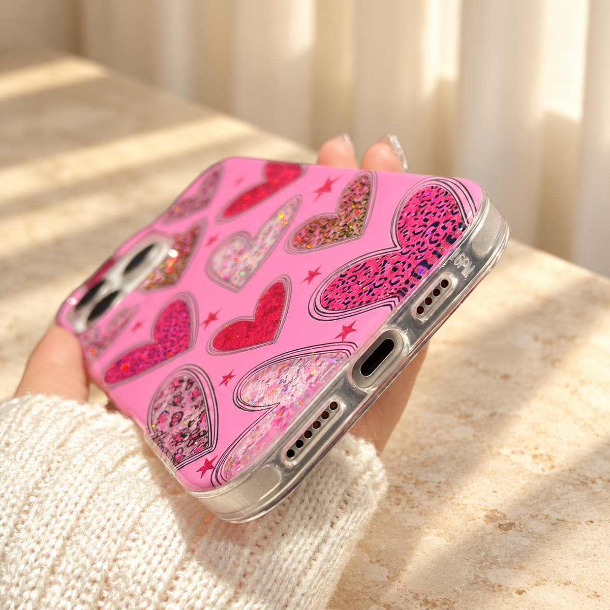 Bottom-angle view of the Valentina Sparkle Heart Pink iPhone case, showing the charging-port and speaker openings in the clear rim.