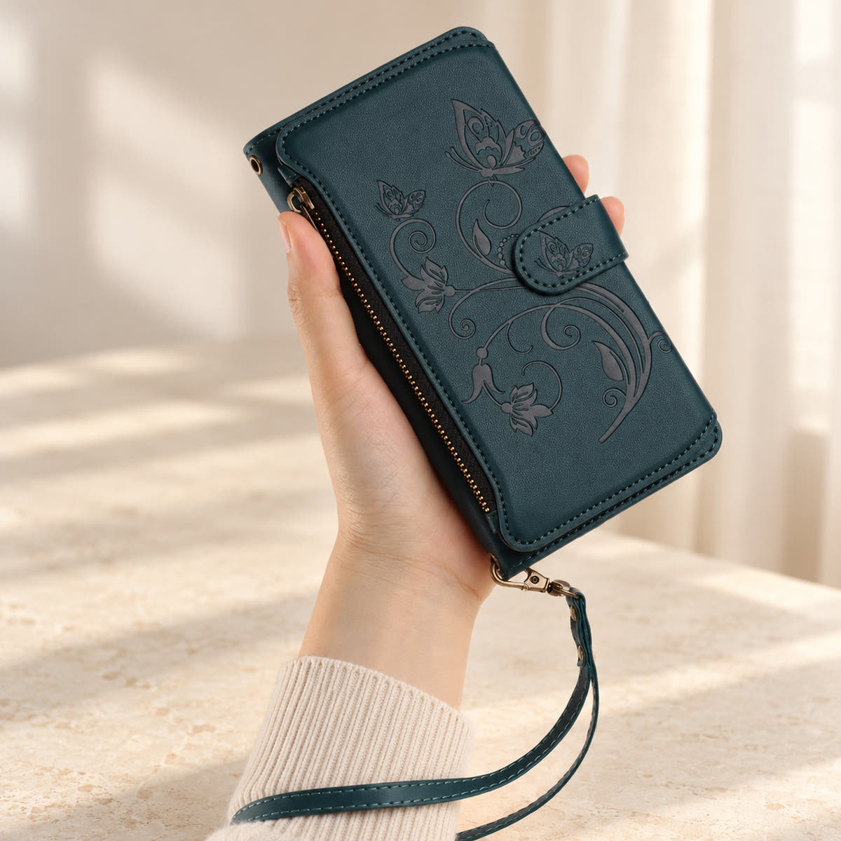 Velora Zip iPhone wallet case in Forest Green, handheld with embossed butterfly front, side zip and matching wrist strap.