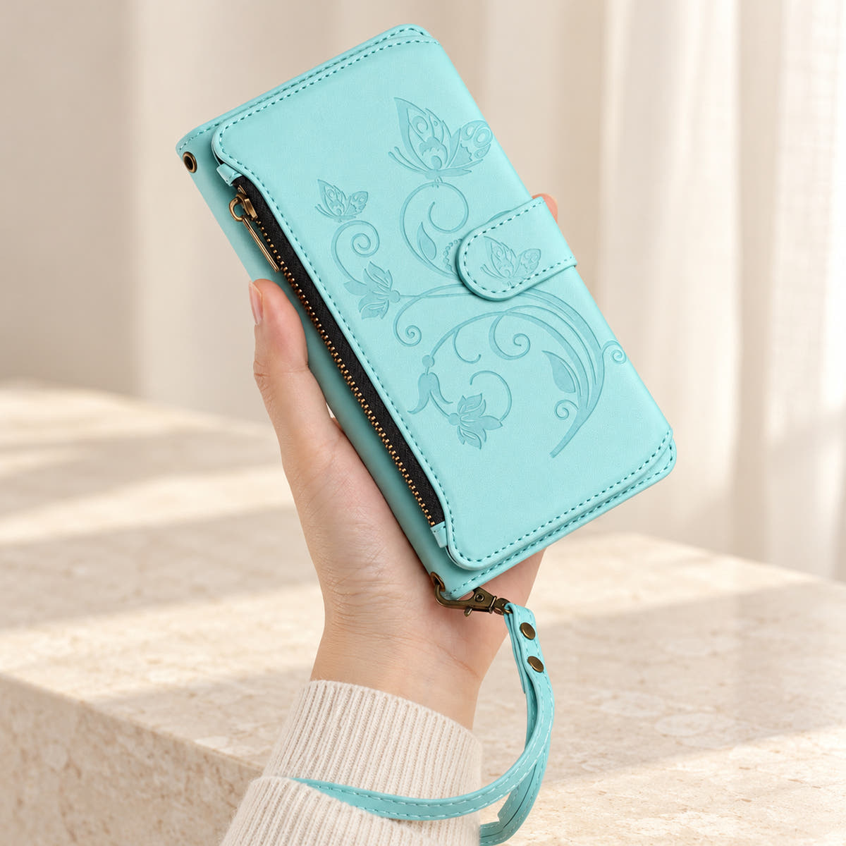 Velora Zip iPhone wallet case in Ice Blue, handheld with embossed butterfly front, side zip and matching wrist strap.