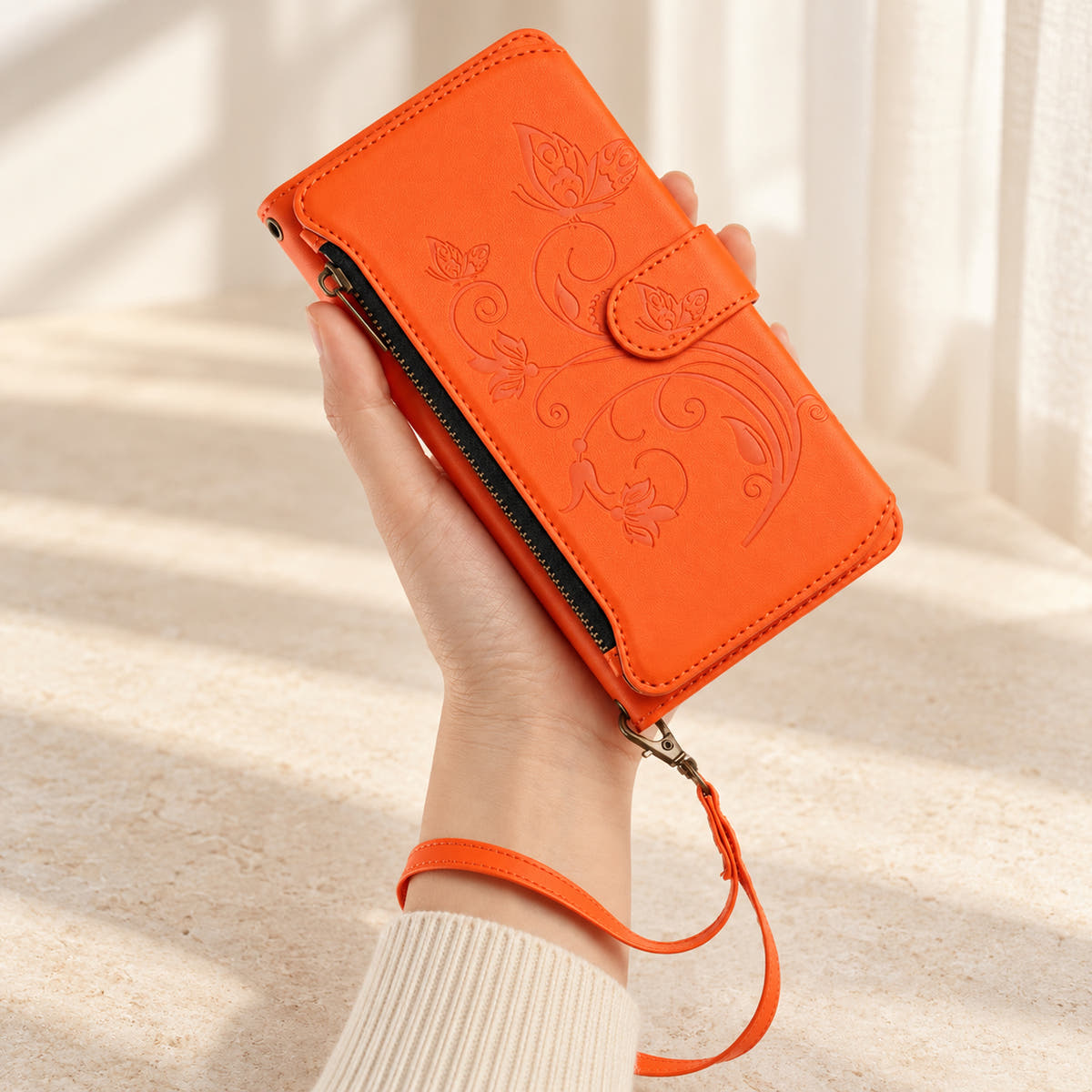 Velora Zip iPhone wallet case in Orange, handheld with embossed butterfly front, side zip and matching wrist strap.