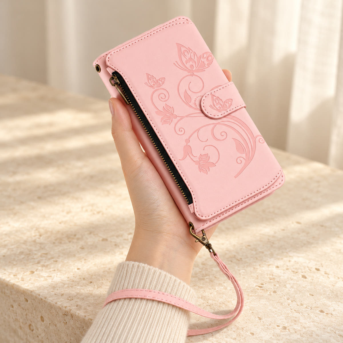 Velora Zip iPhone wallet case in Pink, handheld with embossed butterfly front, side zip and matching wrist strap.