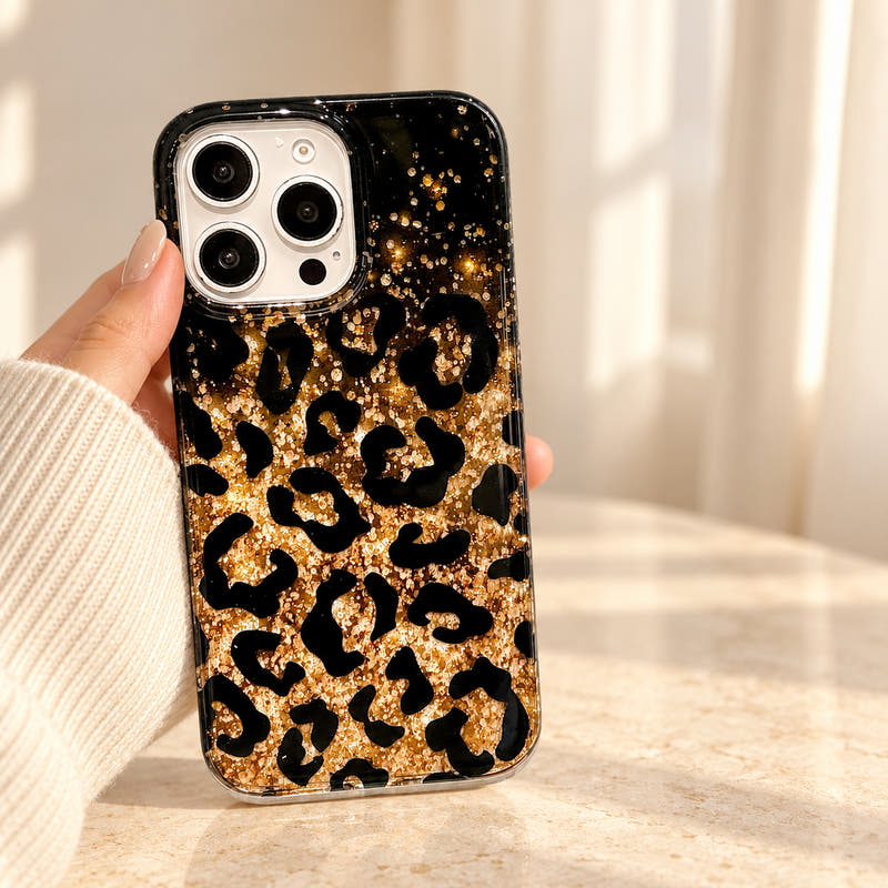 Black Zahara Luxe leopard glitter iPhone case held in a cream-sleeved hand, showing its gold shimmer and dark upper gradient.