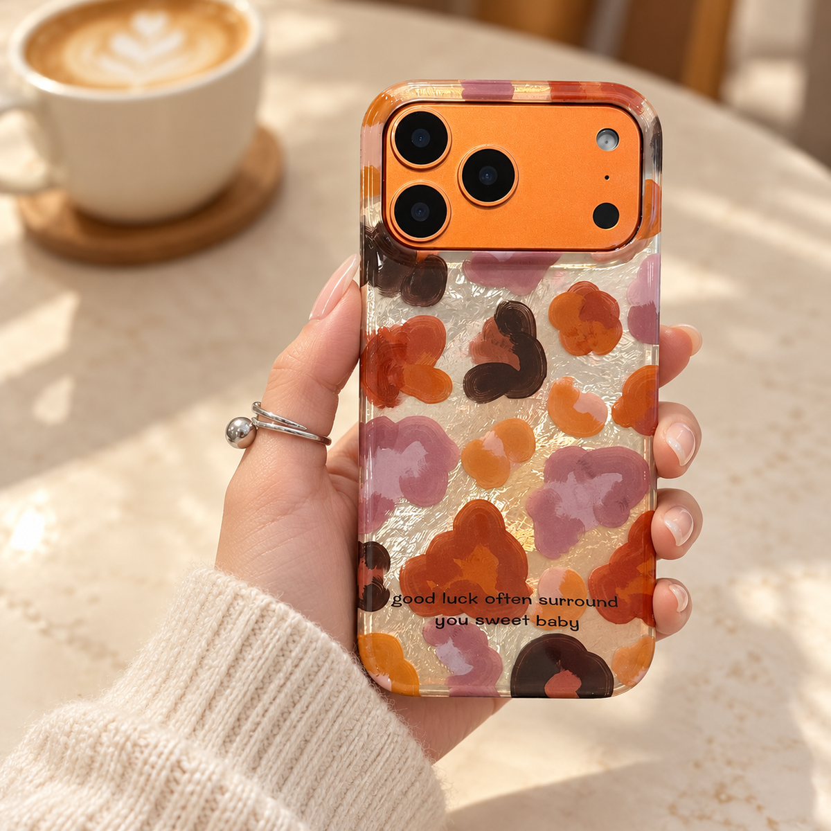 Autumn Mix floral case held above a cream café table with a softly blurred coffee cup in the background.