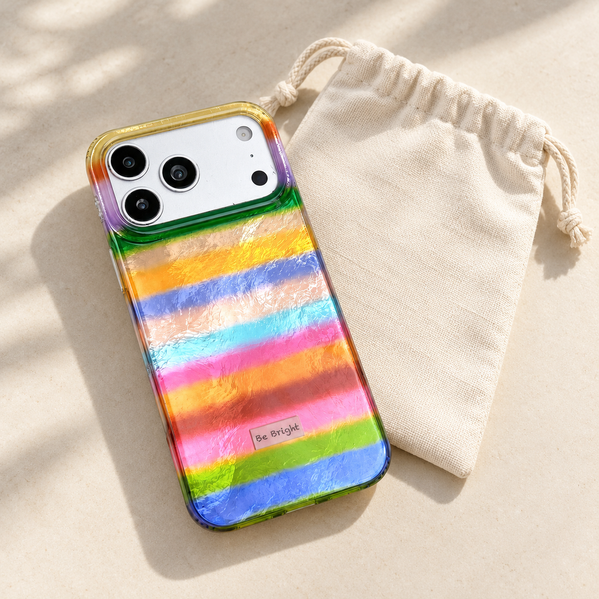 Be Bright rainbow stripe iPhone case — styling beside a cream pouch.
