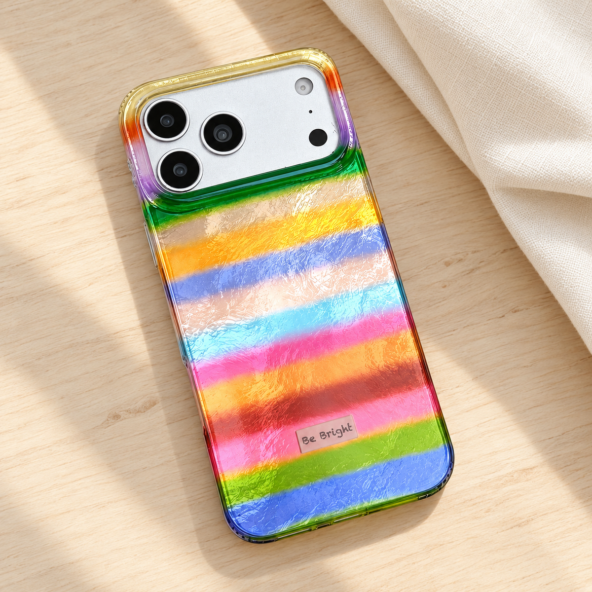Be Bright rainbow stripe iPhone case — diagonal tabletop view.