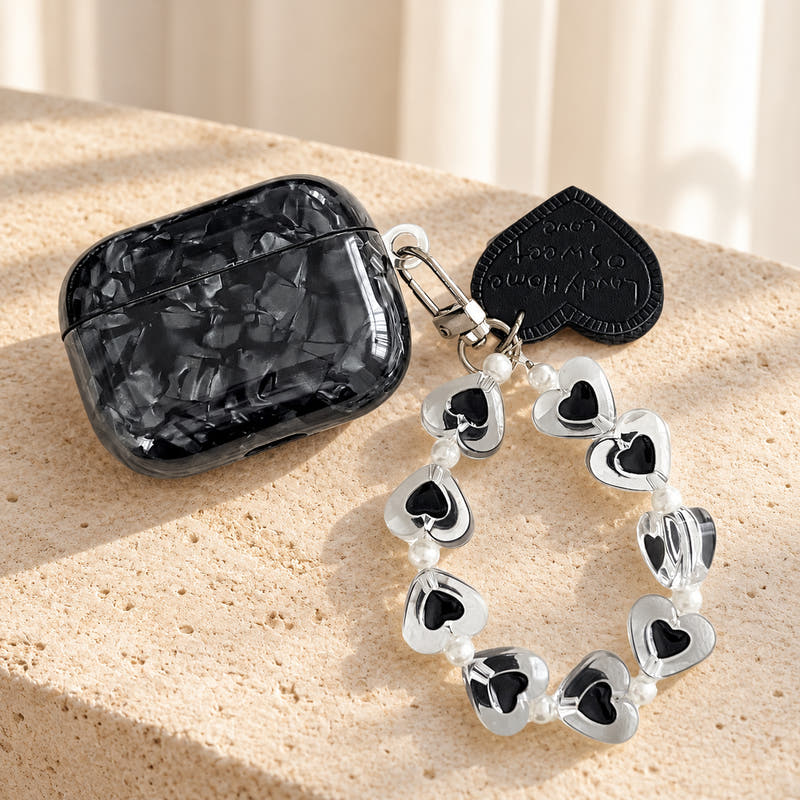 Black Obsidian Marble AirPods Case in Black Obsidian, hero with original attached charms on a warm cream background