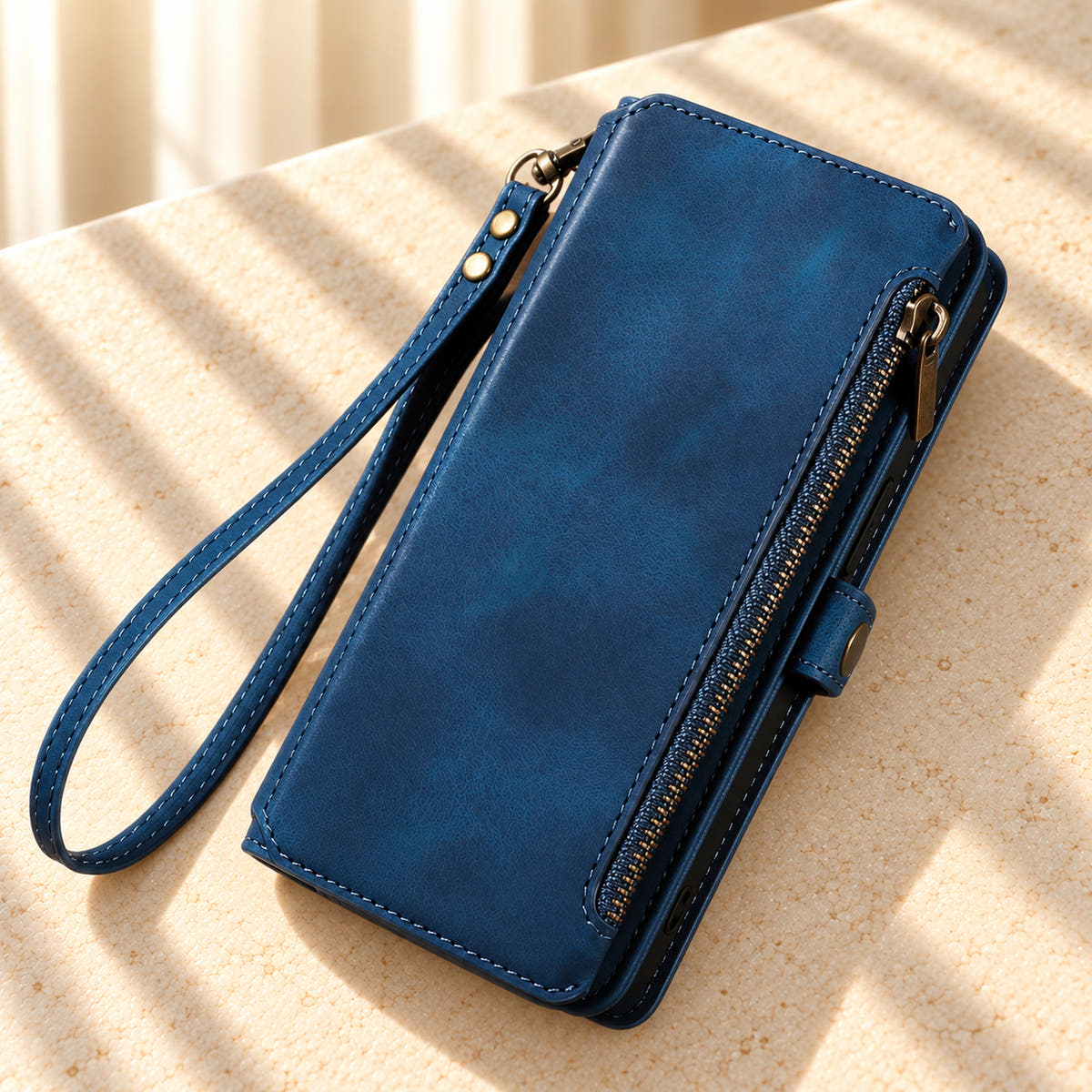 BlushCarry Navy Blue wallet phone case on a sunlit cream tabletop, showing its straight edge zip pocket and matching wrist strap.