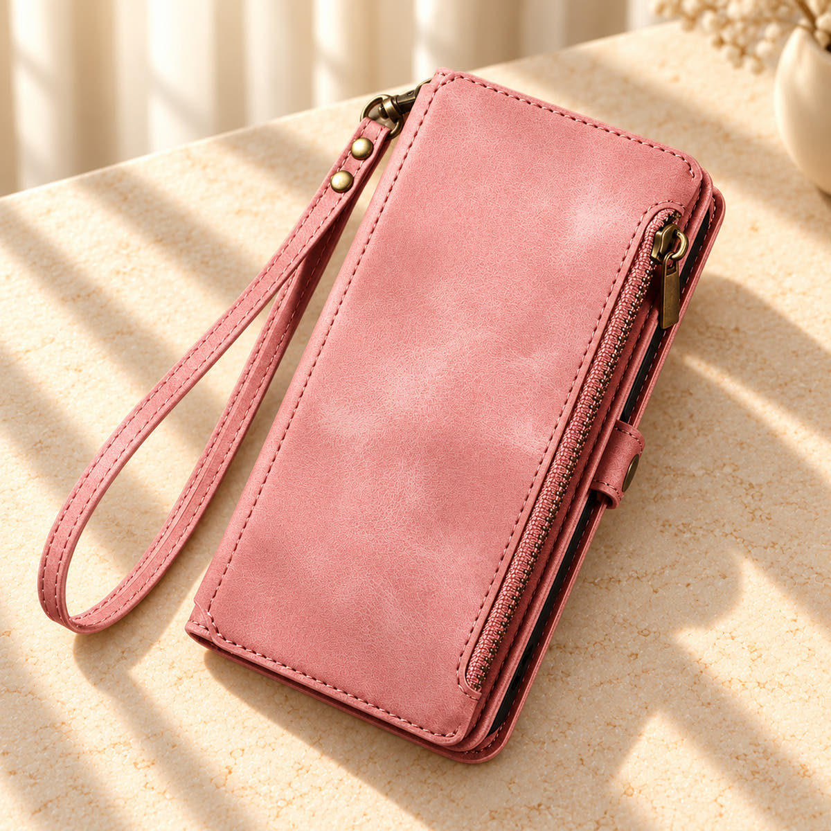 BlushCarry Pink wallet phone case on a cream stone tabletop with its straight edge zipper and detachable matching wrist loop.