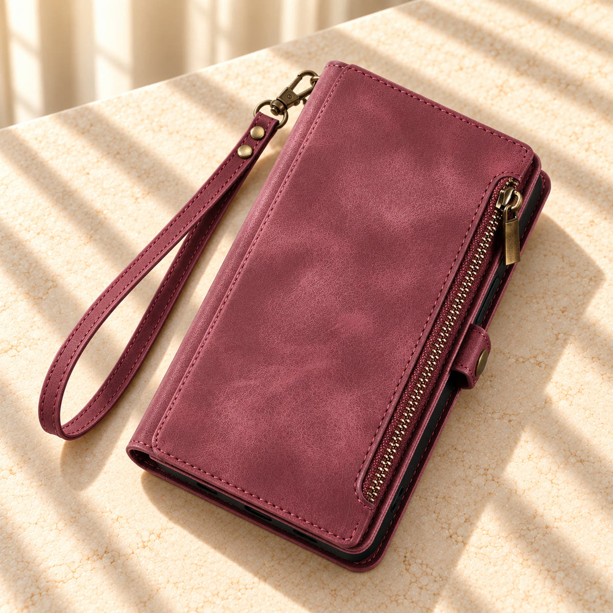 Plum BlushCarry wallet phone case styled diagonally on a sunlit cream tabletop with its edge zip and matching wrist strap.