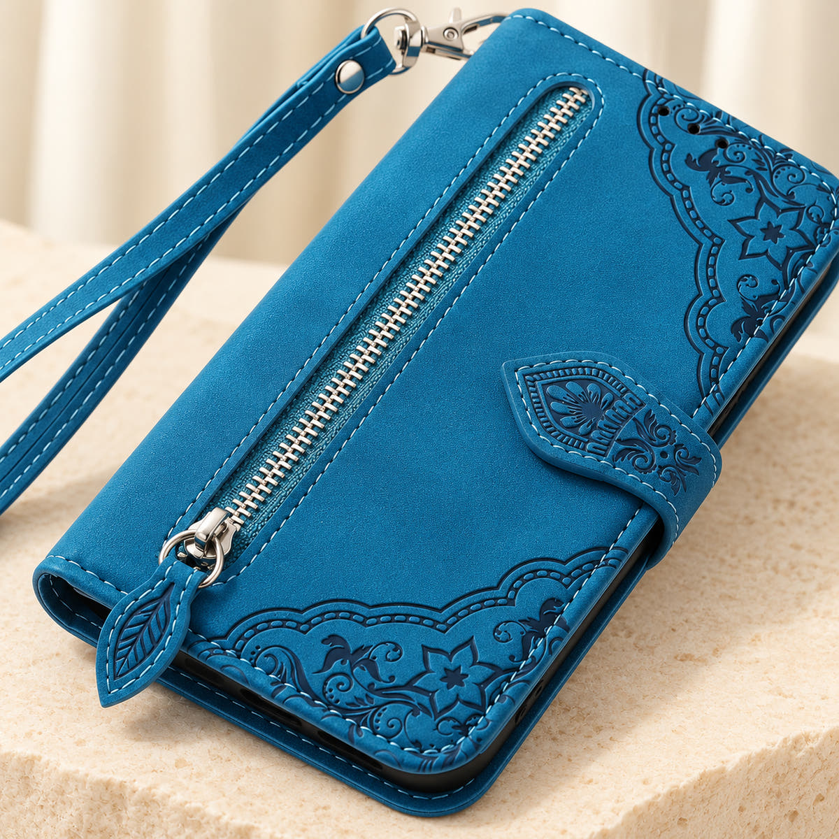Close-up of the Blue Botanical wallet case showing the silver zipper, leaf-shaped pull, embossed floral border and stitching.