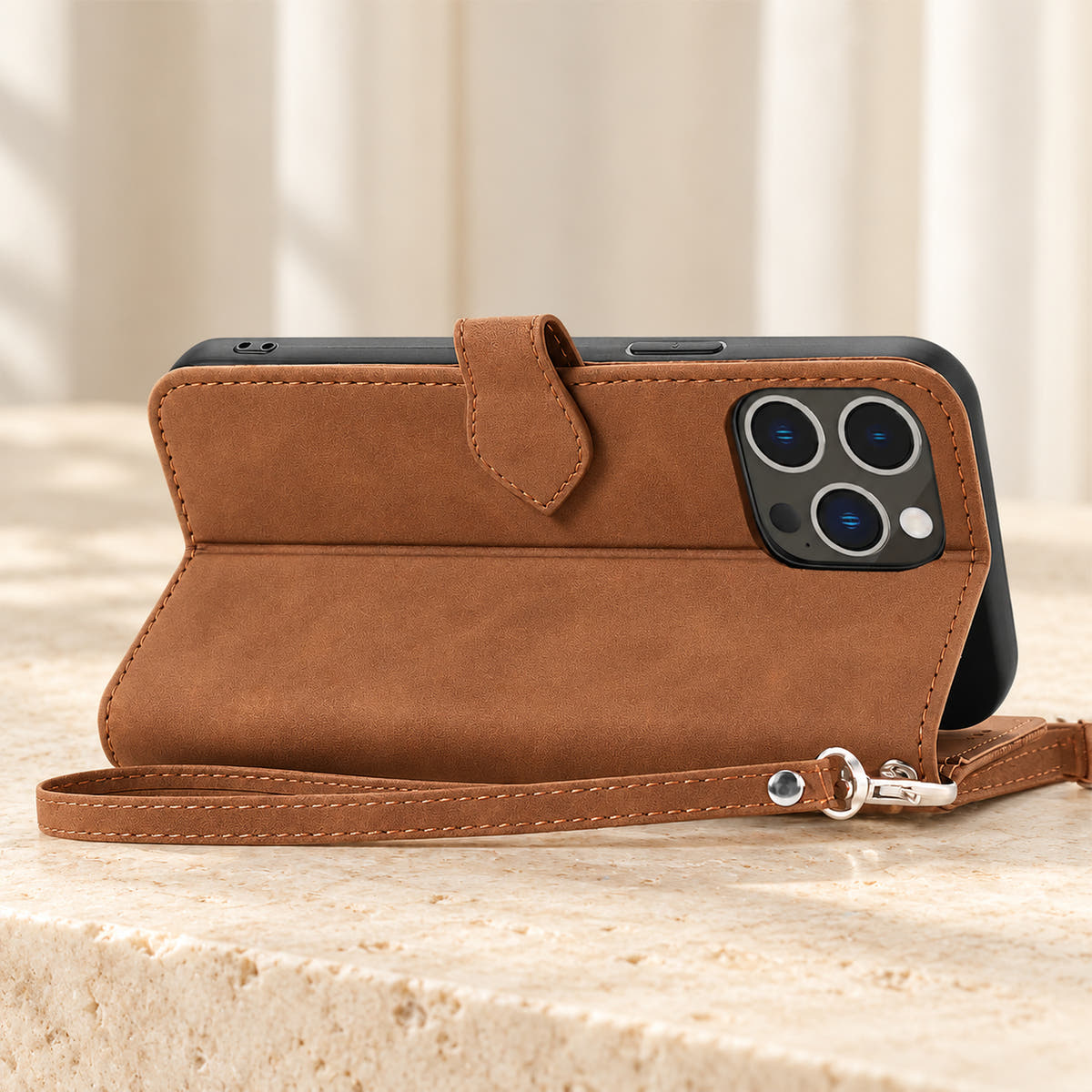 Botanical wallet iPhone case in Brown folded into a landscape stand, rear view showing the plain back, camera opening and matching wrist loop.