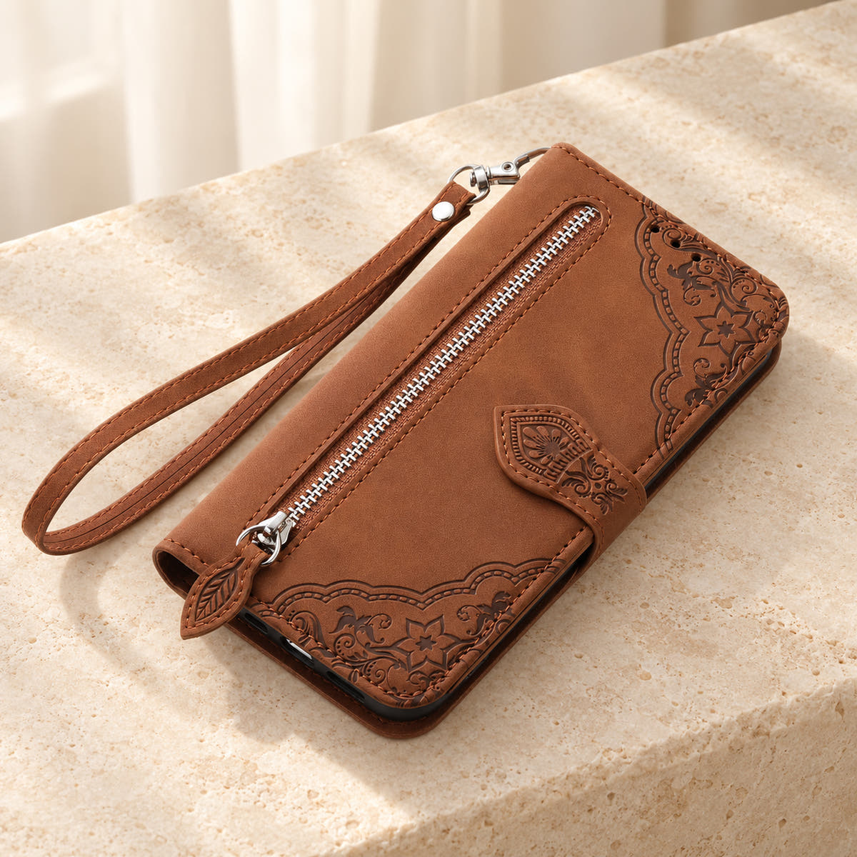 Botanical embossed wallet phone case in Brown, tabletop view of the closed folio with external zip pocket and matching wrist strap.