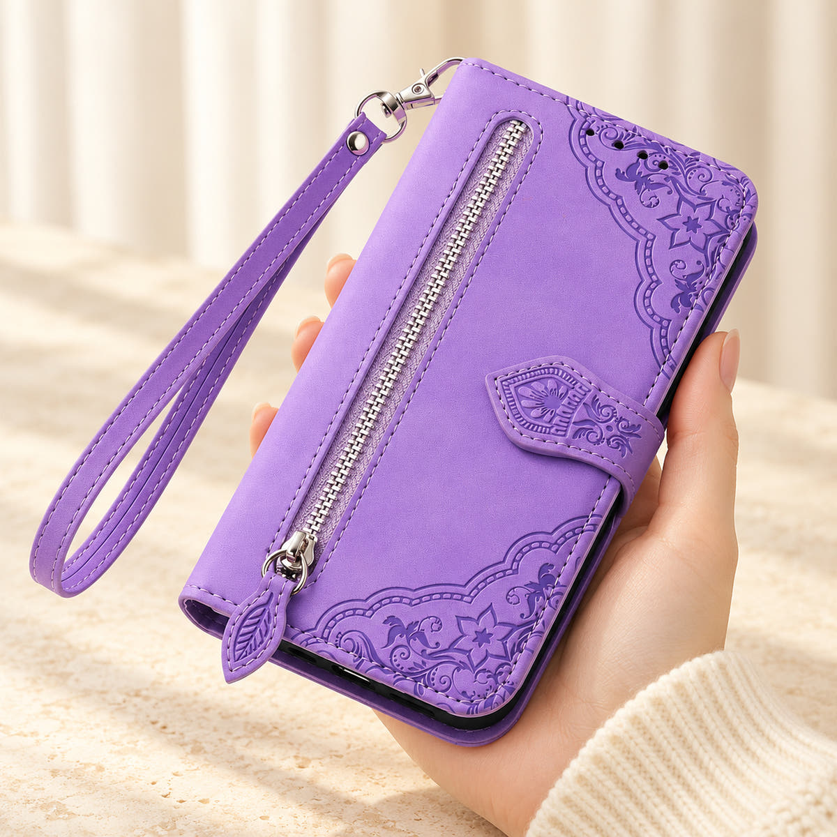 Botanical embossed iPhone wallet case in Lavender, handheld front view with silver zip pocket, leaf-shaped pull and matching wrist loop.