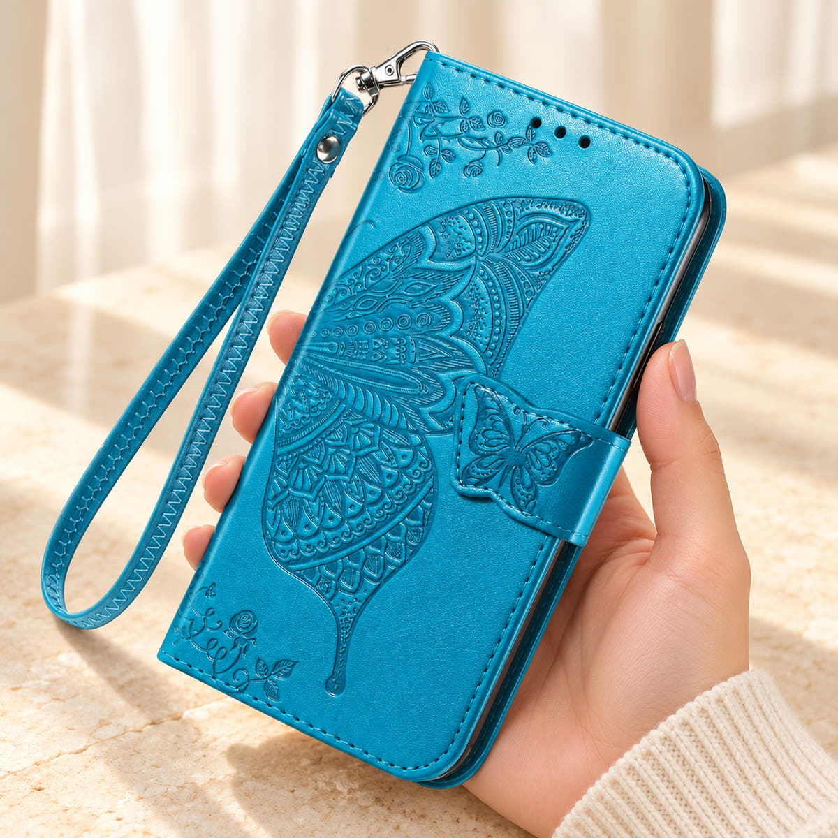 Butterfly embossed iPhone wallet case in Cloud Blue, handheld closed-front view with butterfly tab and matching wrist loop.