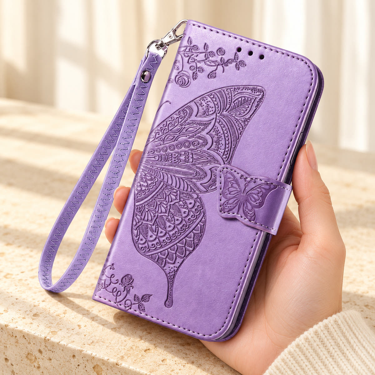 Butterfly embossed iPhone wallet case in Lavender, handheld closed-front view with butterfly tab and matching wrist loop.
