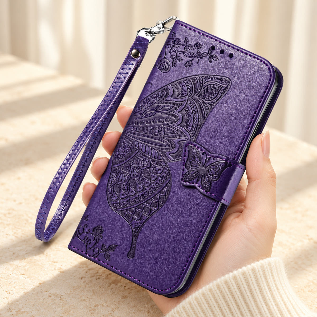 Butterfly embossed iPhone wallet case in Purple, handheld closed-front view with butterfly tab and matching wrist loop.