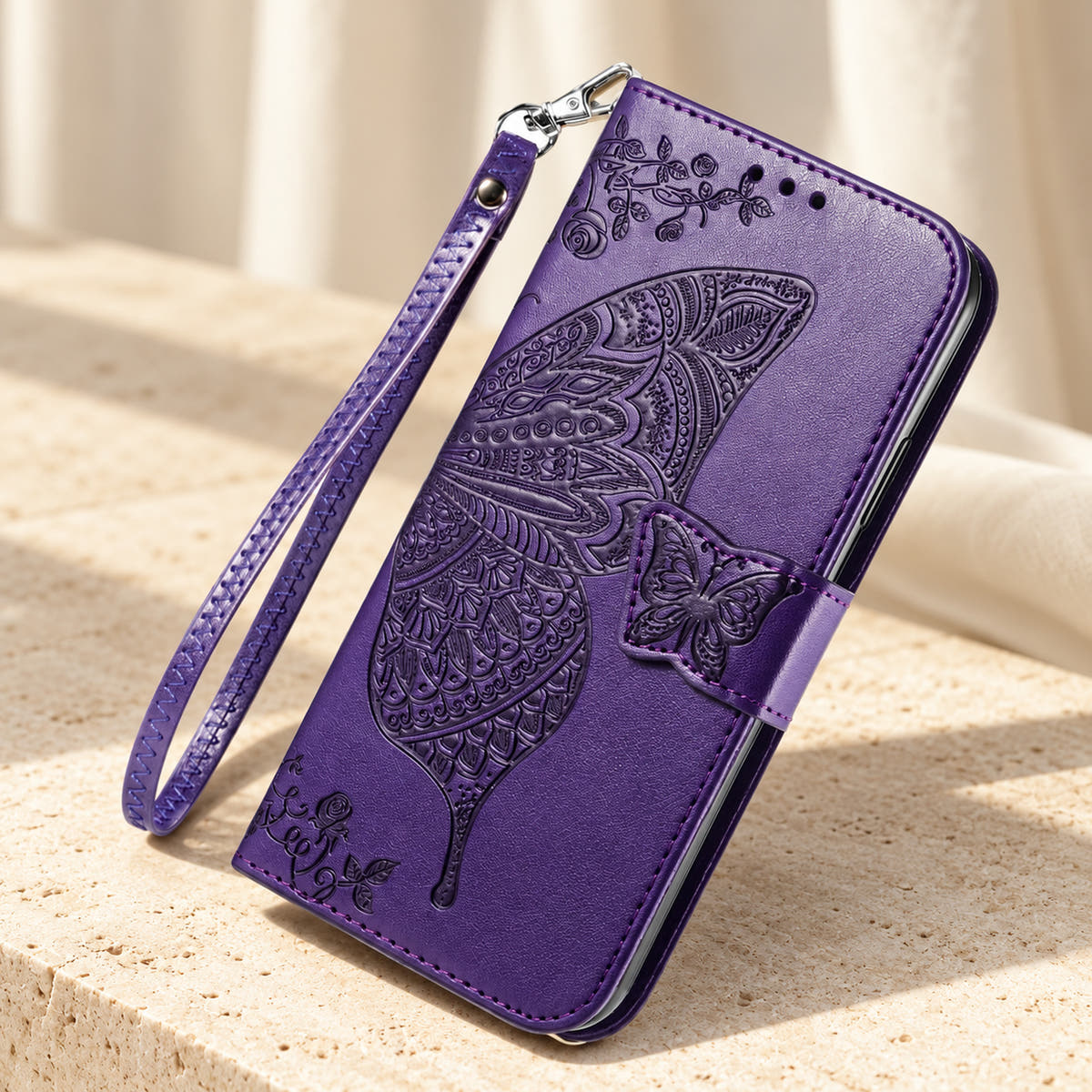 Butterfly embossed iPhone wallet case in Purple, tabletop front view showing the detailed wing, tab closure and clip-on wrist loop.